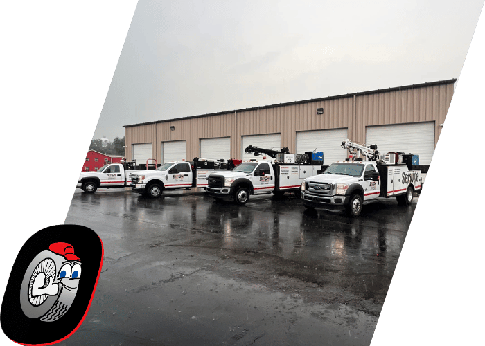Fleet of commercial utility service trucks parked outside a repair facility on a rainy day.