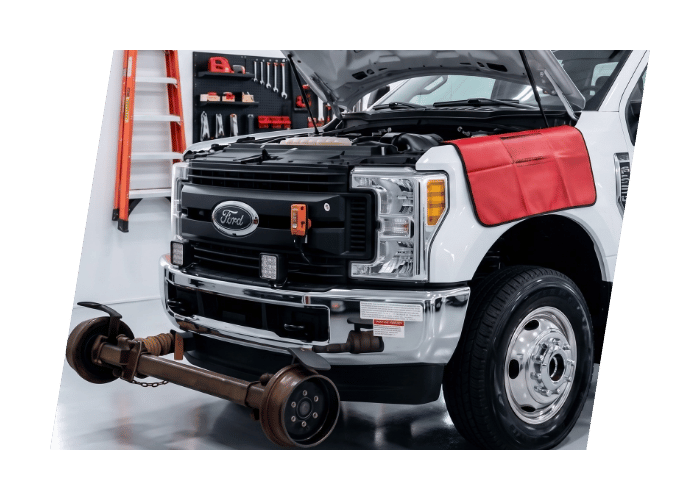 Heavy duty service truck undergoing repair in a commercial shop with the front axle removed.
