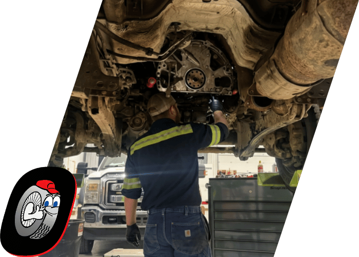 Technician performing drivetrain repairs beneath a lifted commercial truck in a repair shop.