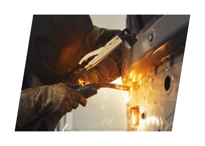 Technician performing welding repairs on a commercial vehicle body with sparks visible during fabrication.