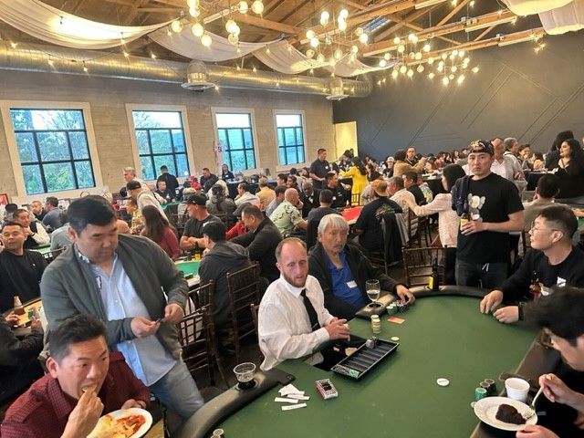 A large group of people are sitting around a poker table.