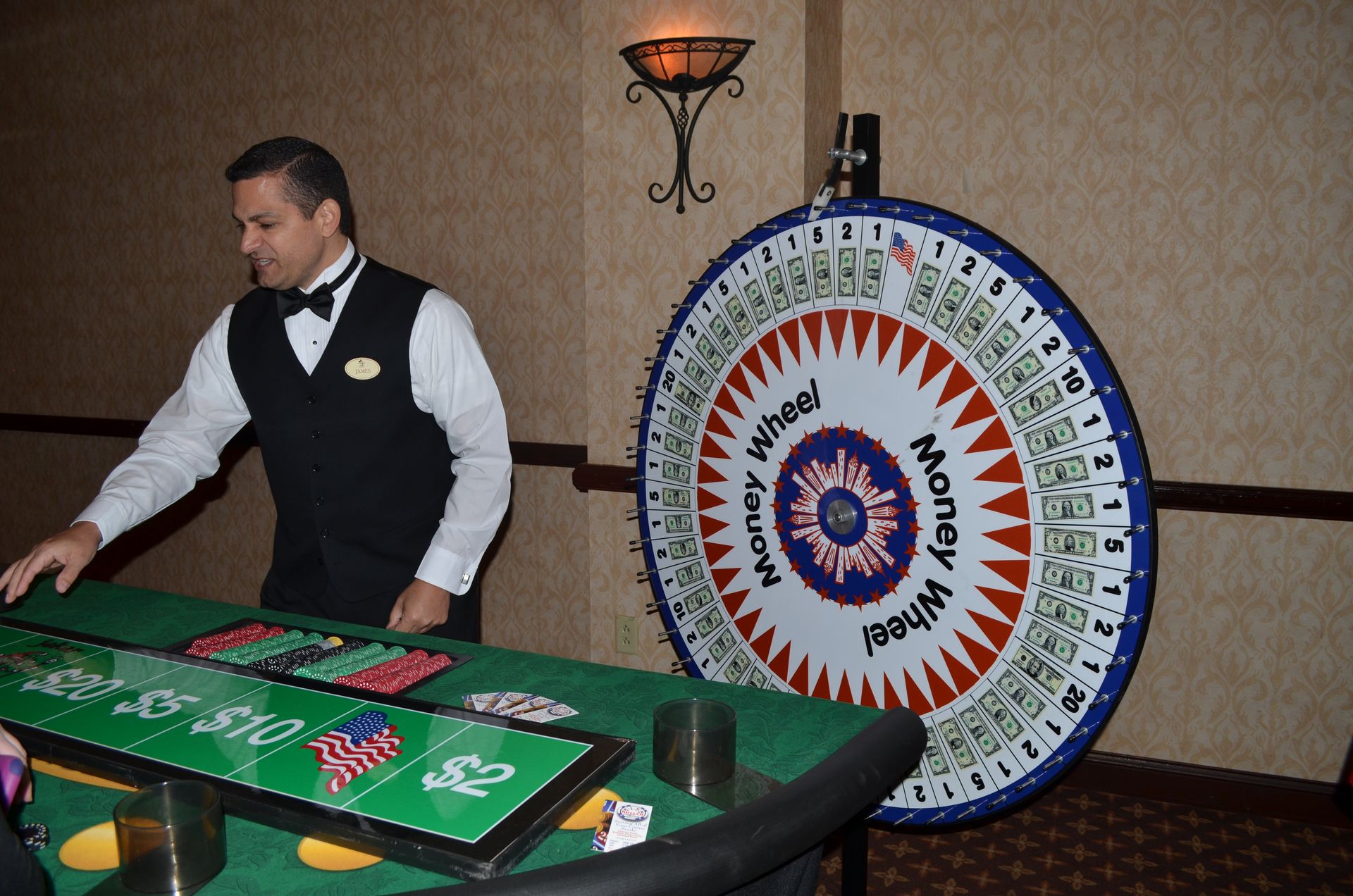 A man in a tuxedo stands in front of a money wheel