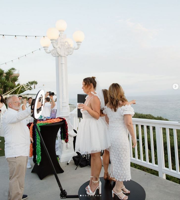 Two people in white dresses at an outdoor seaside party beside a decorated table and lamp post