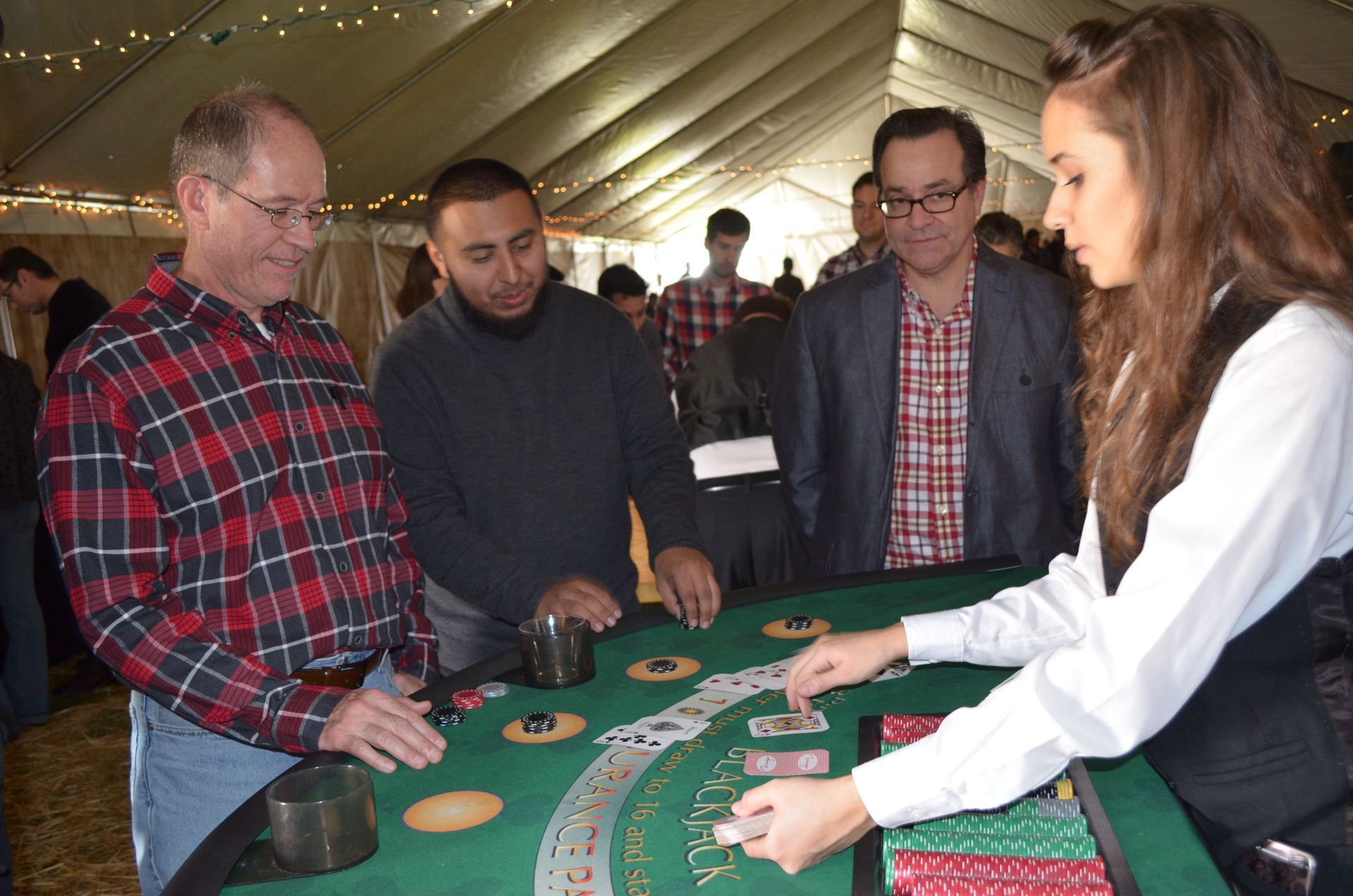 People gathered around a casino table, with a dealer handling cards and chips under a tent.