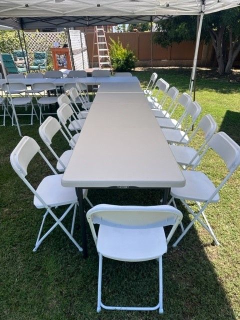 Long banquet table with white folding chairs under a canopy on a grassy lawn.