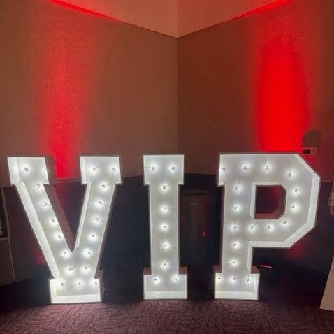 Large white lighted “VIP” letters on a carpeted floor with red ambient lighting in a room