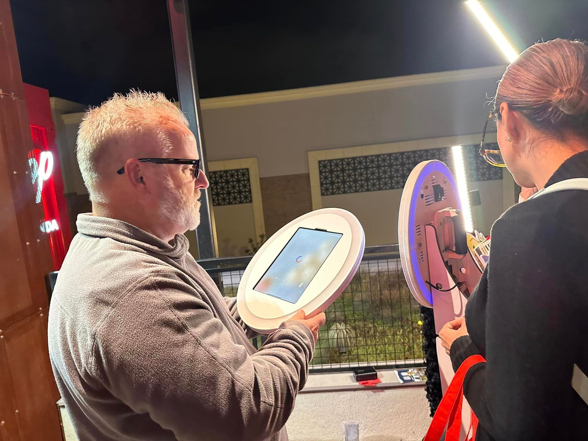 Two people holding illuminated handheld mirrors outdoors at night under a bright lamp.