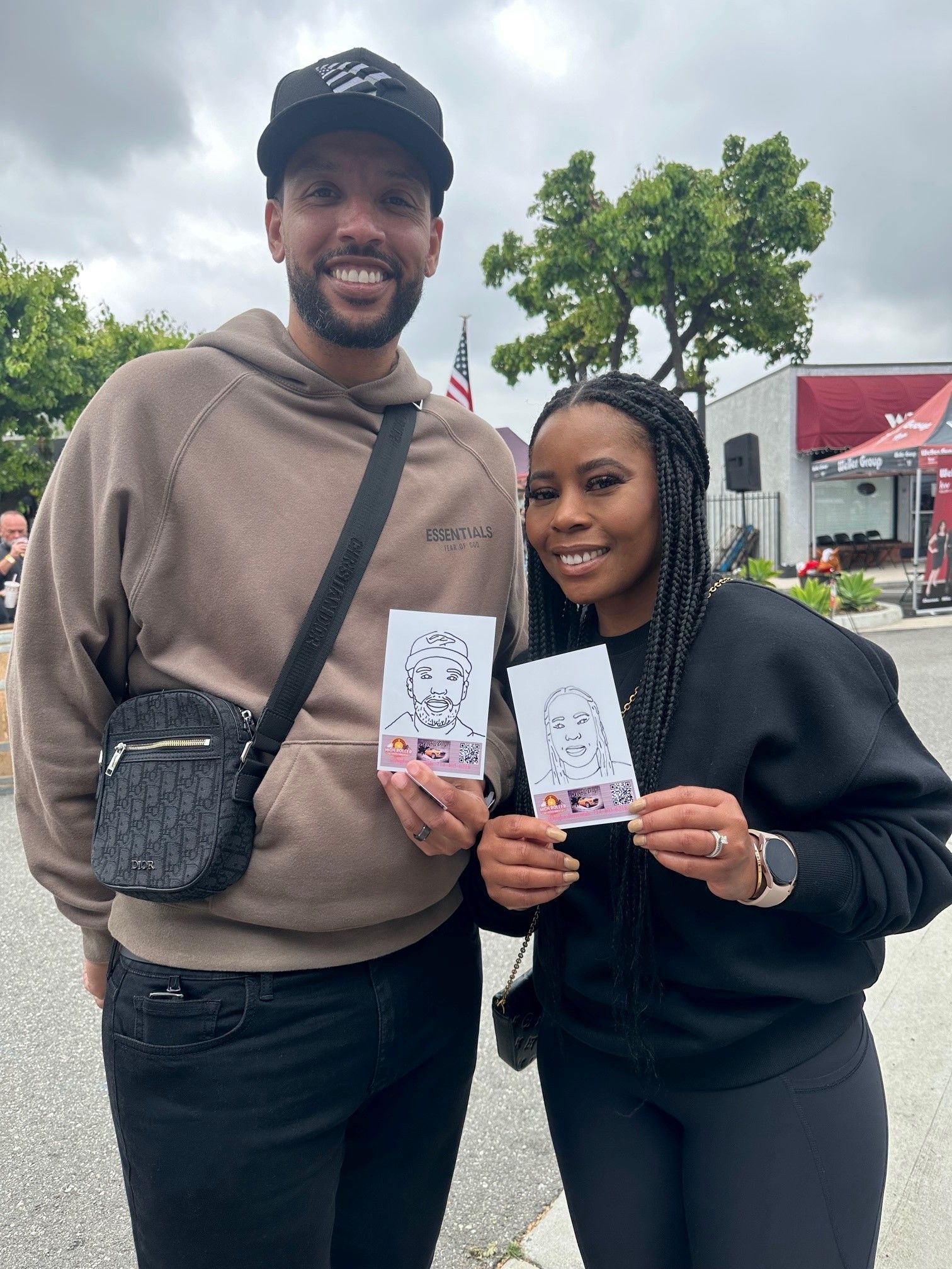Two people smiling outdoors, holding tickets in a park-like area on an overcast day