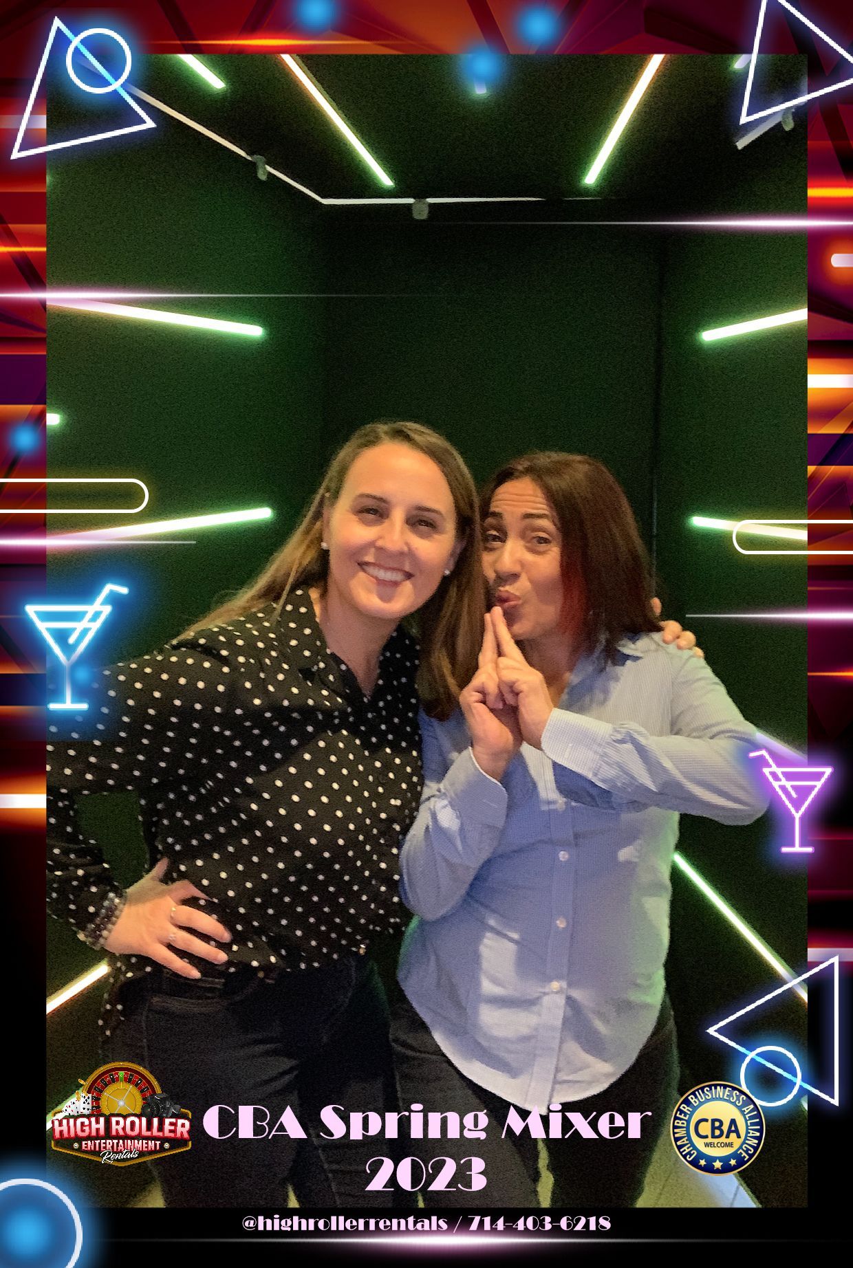 Two smiling people pose in front of neon lights, one making a peace sign, at an event photo backdrop.