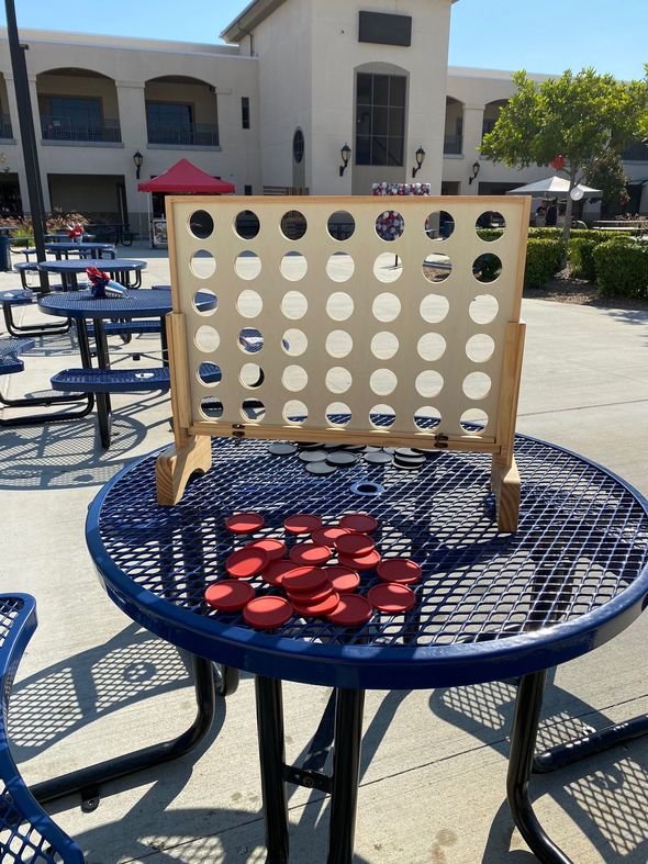 Connect Four game on a blue patio table outdoors with red and black discs stacked below.