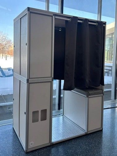 Compact privacy booth with open curtain panels and a small lower compartment in a bright lobby