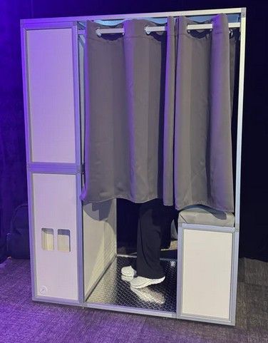 Person standing inside a purple photo booth with curtains drawn aside