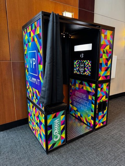 Colorful VIP photo booth kiosk in a hallway, with geometric rainbow panels and a black curtain.