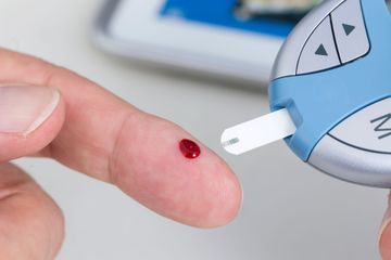 Finger mit einem Blutstropfen neben einem Blutzuckermessgerät-Teststreifen