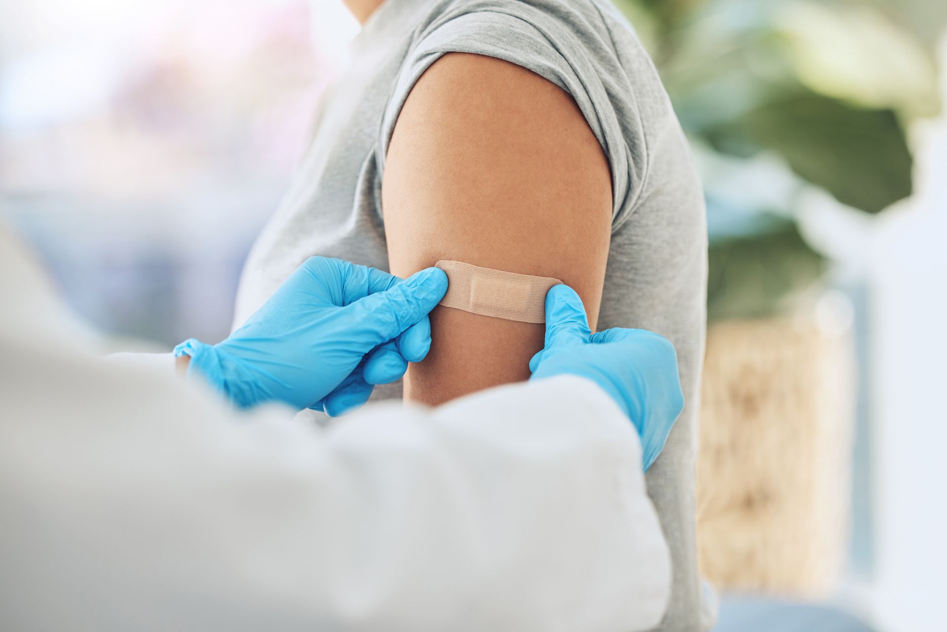 Eine medizinische Fachkraft klebt einem Patienten ein beigefarbenes Pflaster auf den Oberarm.