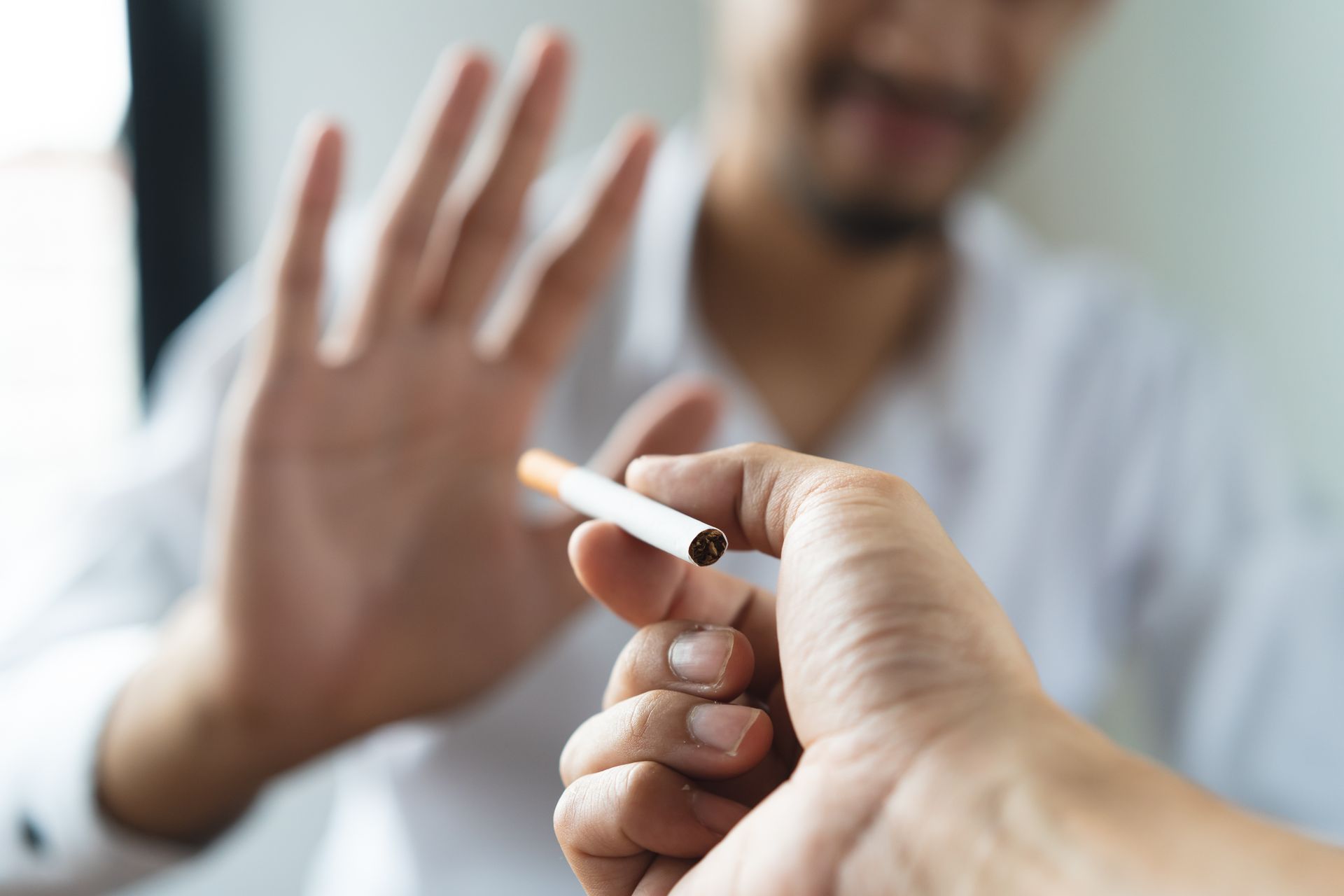 Eine Hand hält eine Zigarette in Richtung einer Person, die eine Stoppgeste macht.