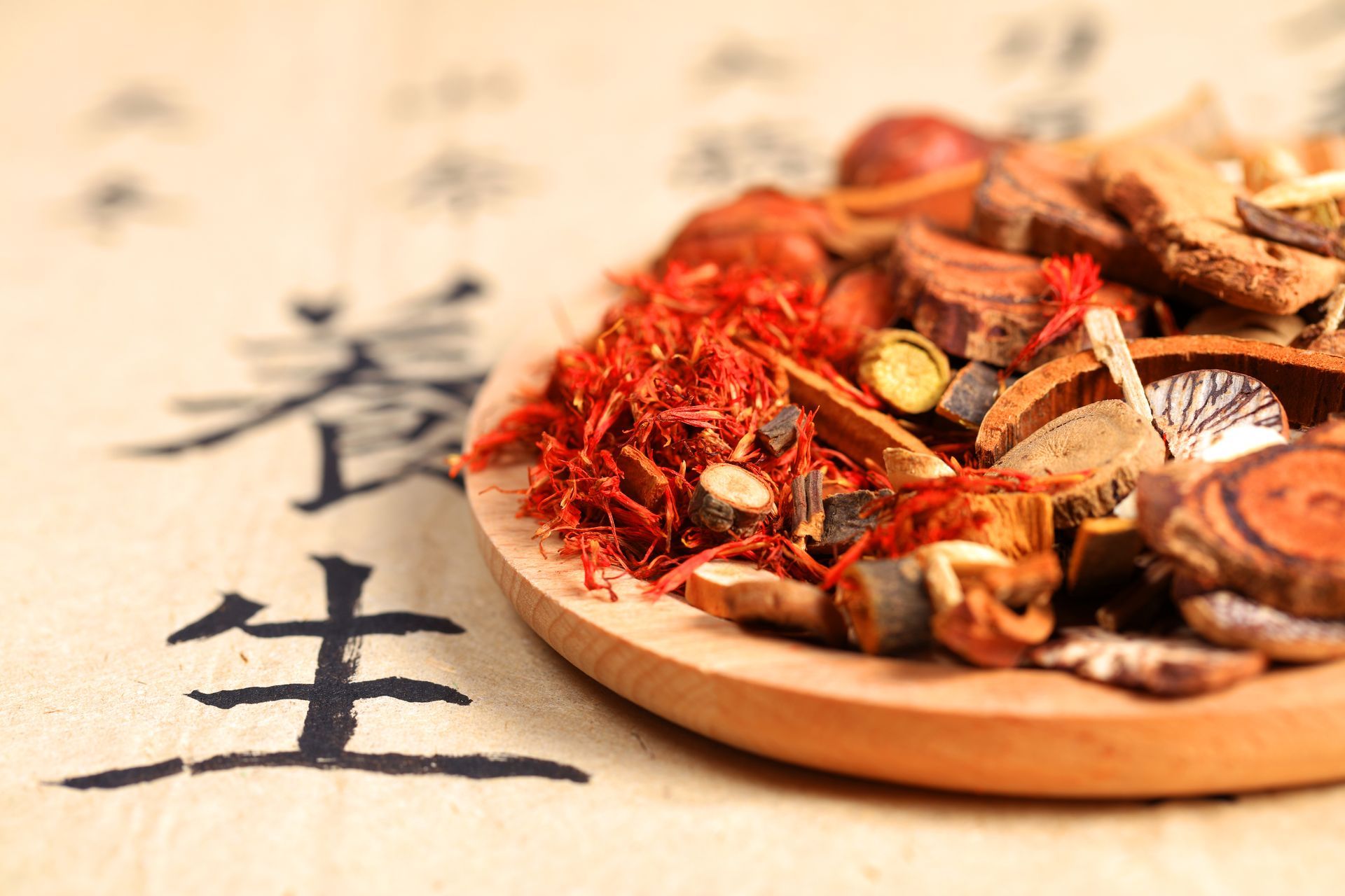 Verschiedene getrocknete Kräuter und Gewürze in einer Holzschale neben chinesischen Schriftzeichen auf Pergament