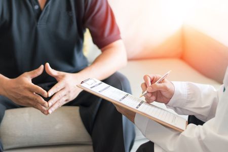 A practitioner is talking to a patient while holding a clipboard.