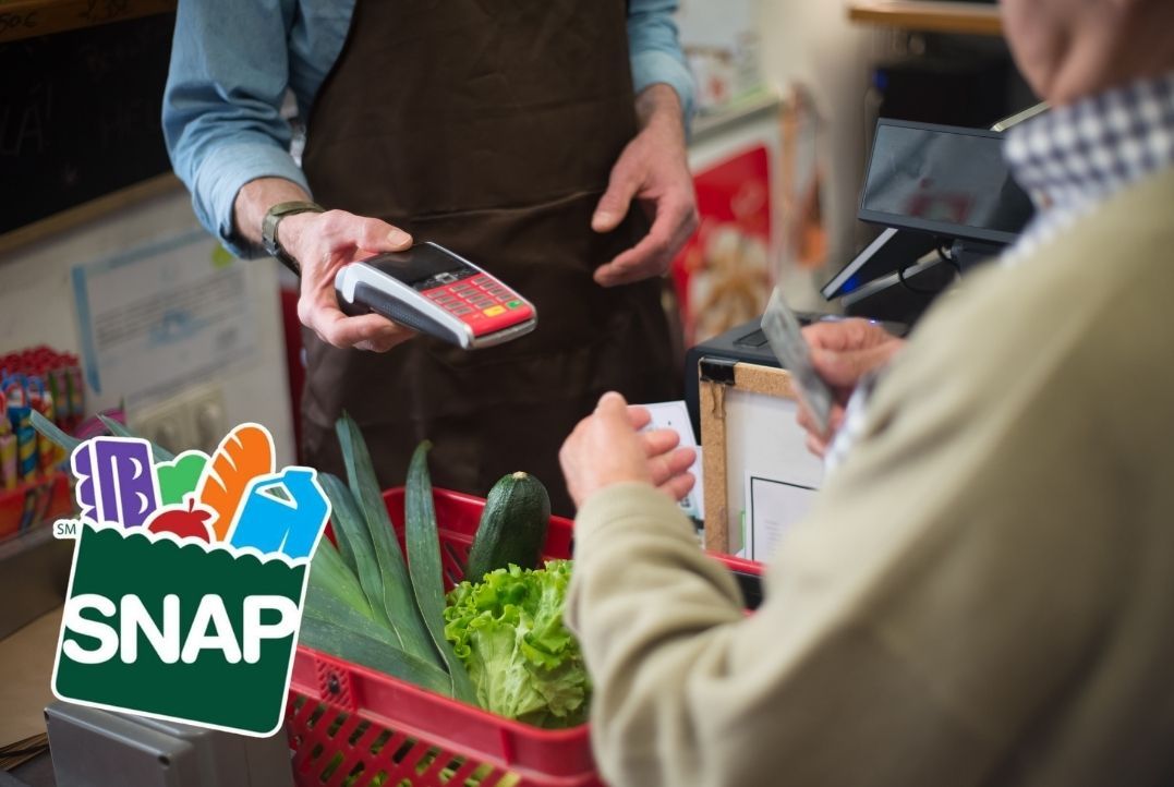 A photo of a customer checking out at a grocery store with a basket full of vegetables.