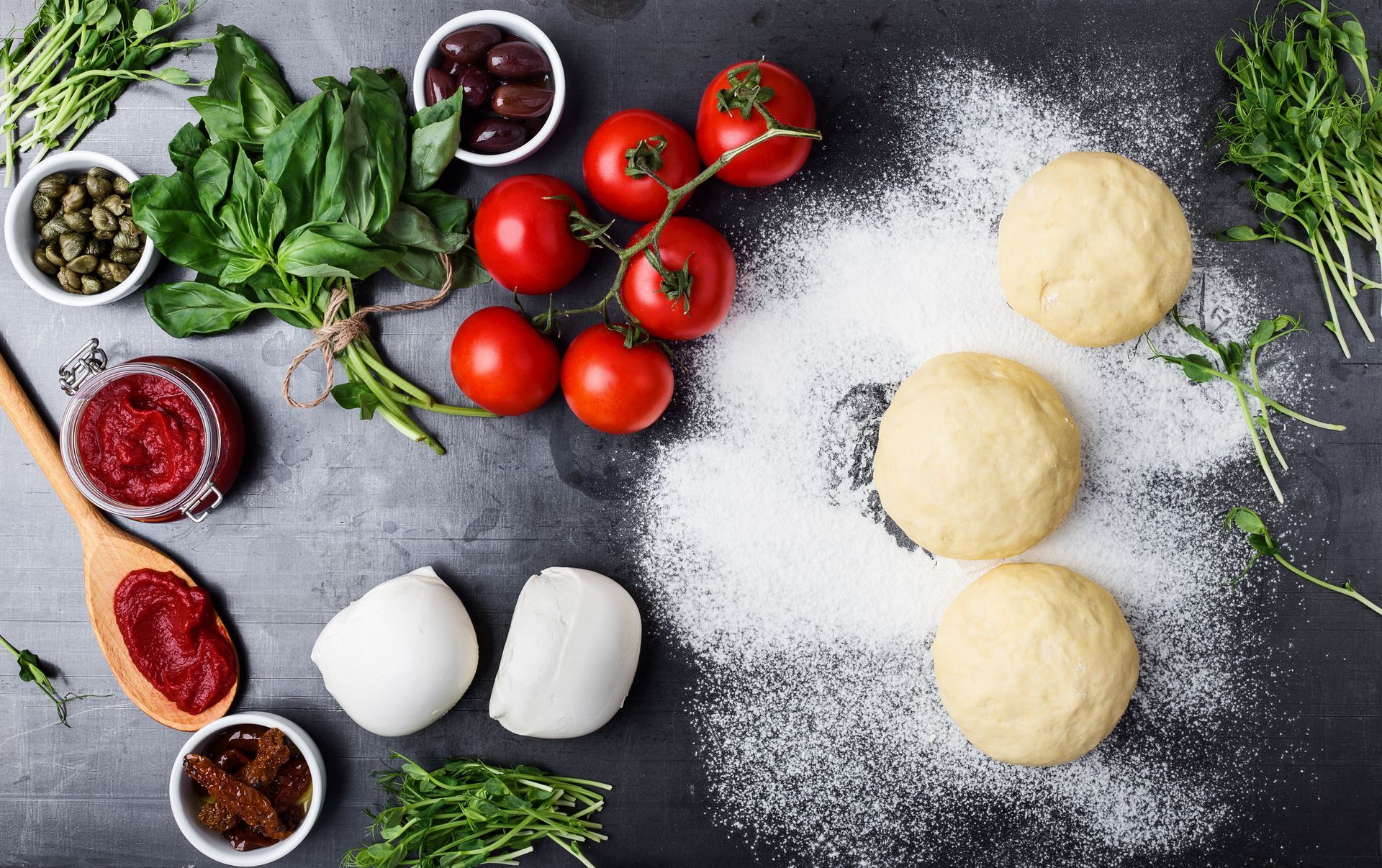 Un tavolo ricoperto di pasta, pomodori, olive e altri ingredienti per la pizza.