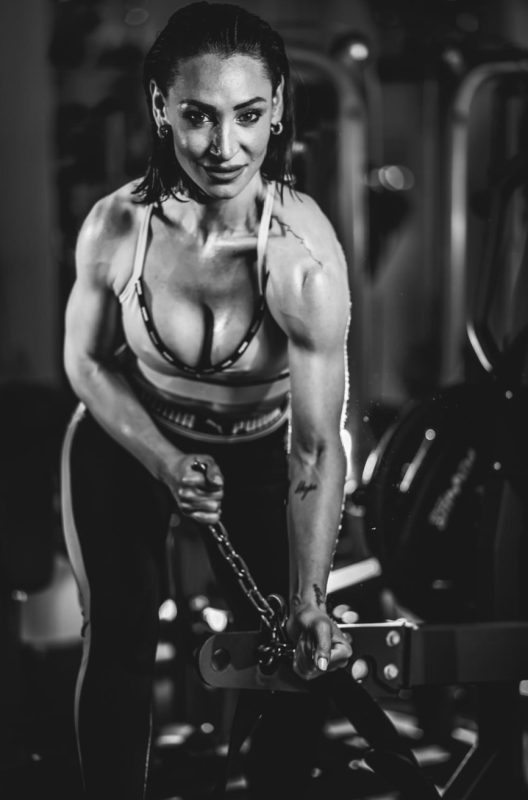 Una donna esegue un esercizio di rematore con i cavi in palestra, impugnando la maniglia con un'espressione concentrata.