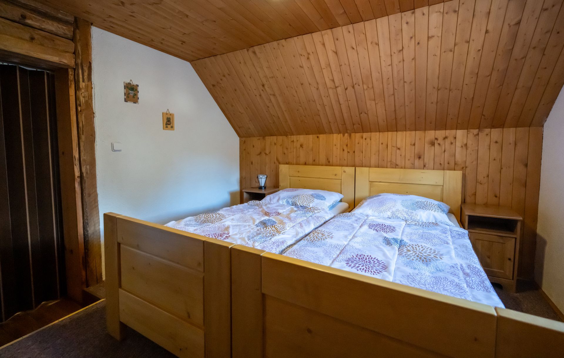 Drevenou obloženou spálňou s manželskou posteľou, šikmým stropom a rustikálnym dekorom