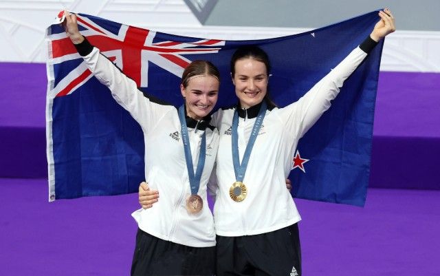 Two female athletes holding a New Zealand flag and medals in their hands