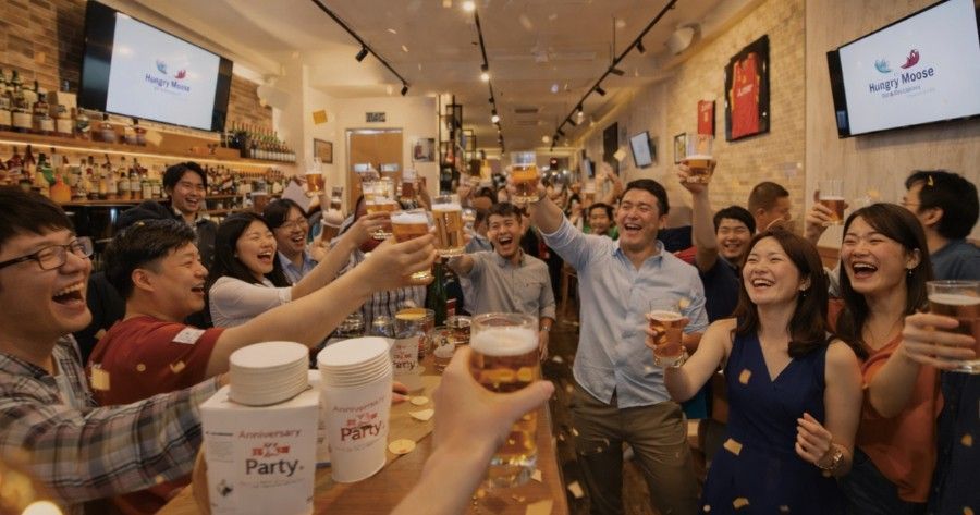 People toasting beer at a bar, confetti flying, bottles in the foreground.
