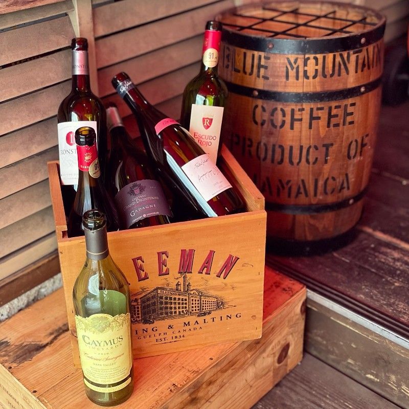 A wooden crate full of bottles of wine, in front of a barrel.