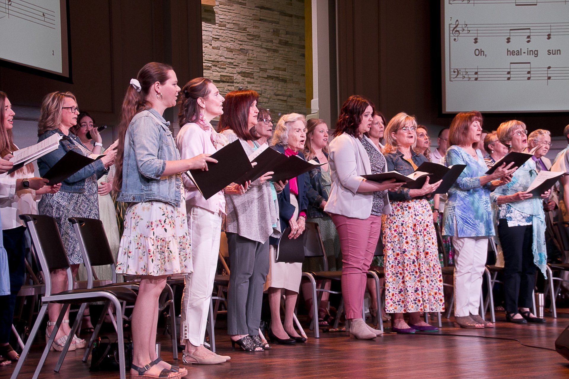A large group of women are singing in a choir on a stage.