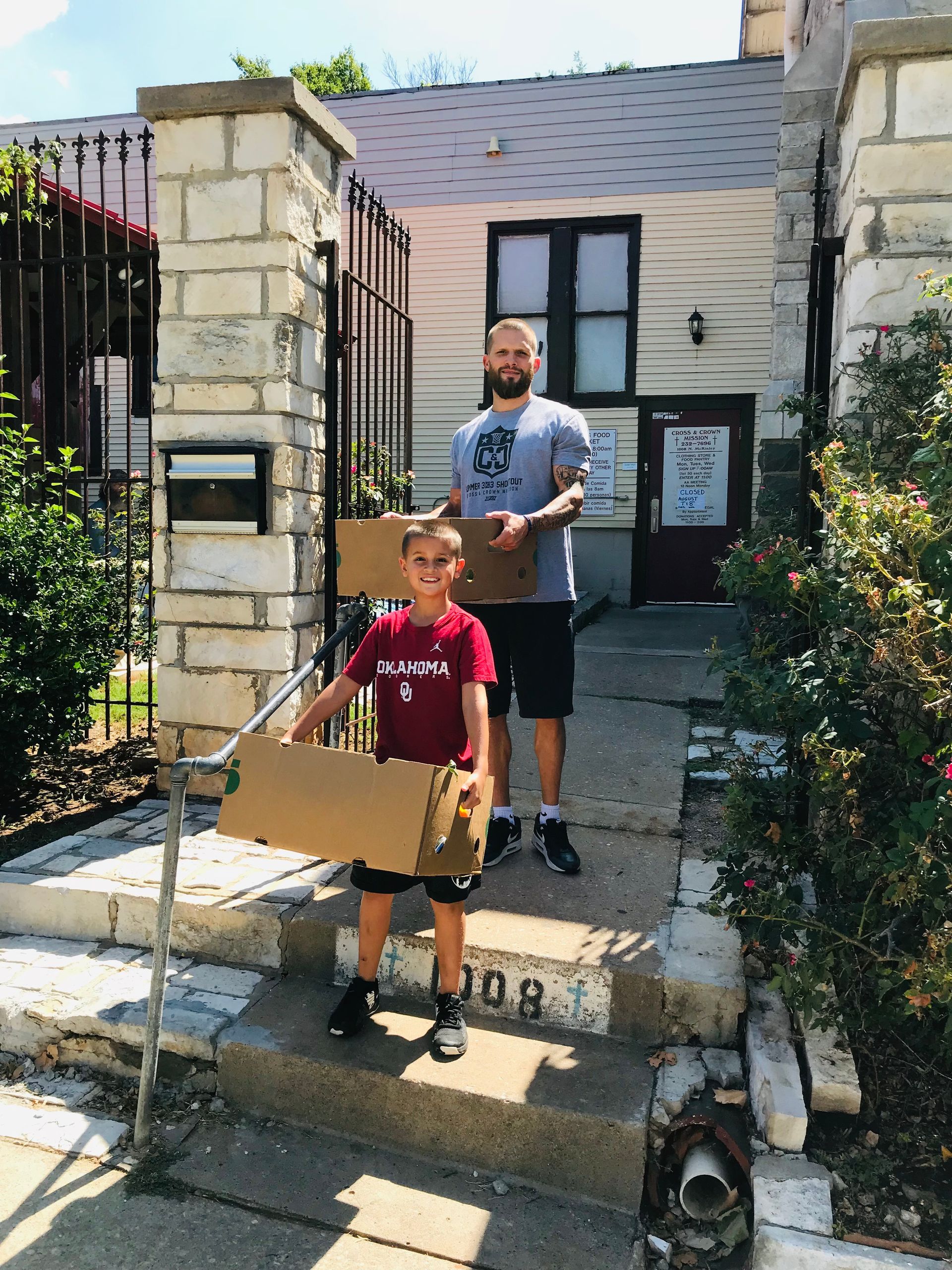 A man and a boy are holding cardboard boxes in front of a house.