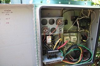 Open electrical control panel with wires, gauges, switches, and circuit components inside a metal box