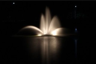 Illuminated fountain jets spraying at night, reflected on calm water