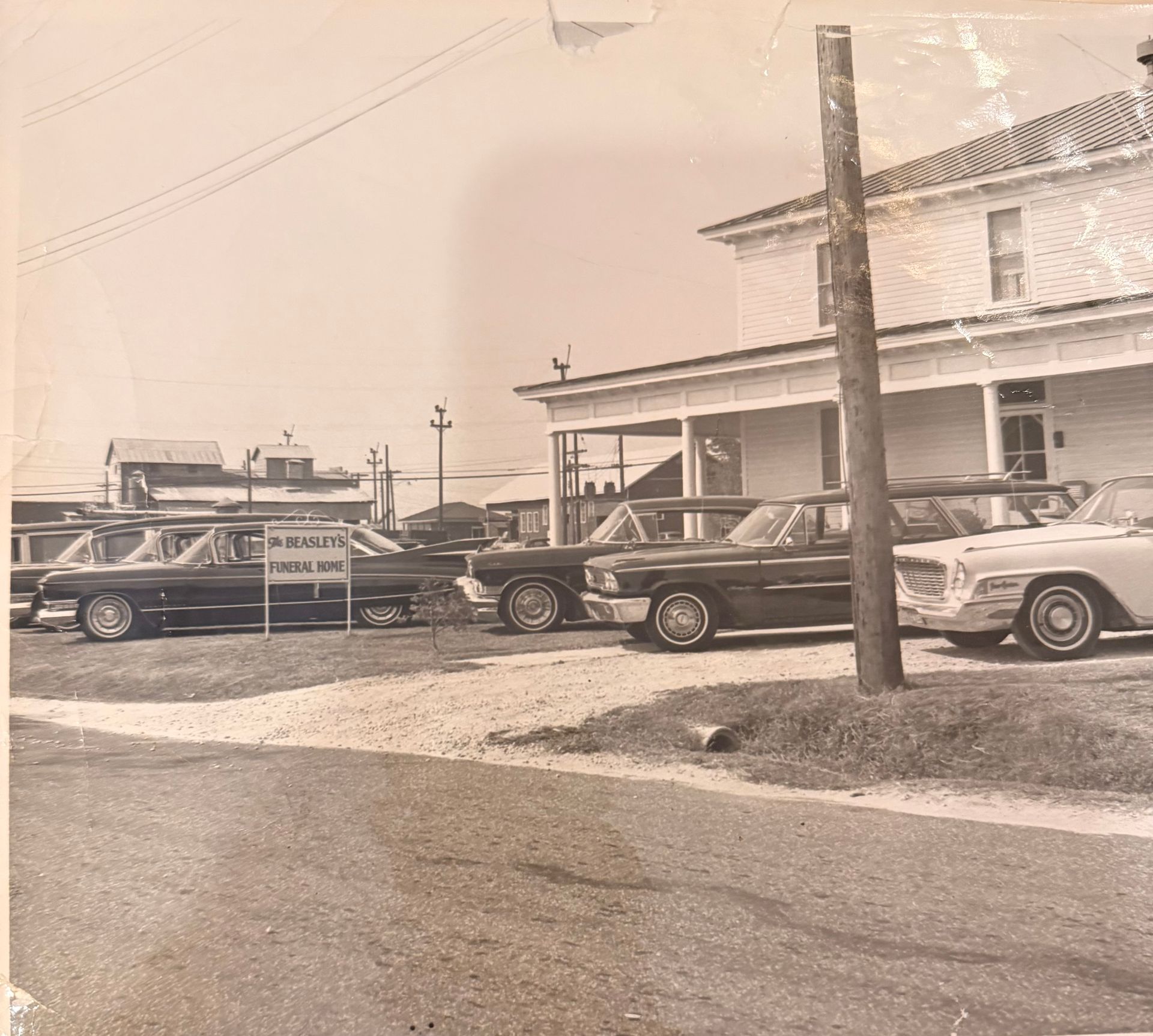 Vintage cars parked outside a small roadside building on a quiet street, seen in sepia tone.