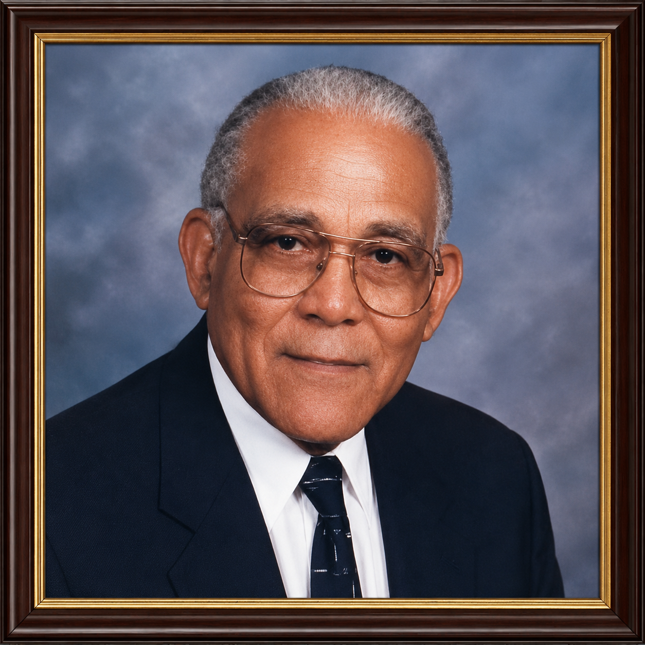 Framed studio portrait of an older man in a dark suit, tie, and glasses against a blue backdrop