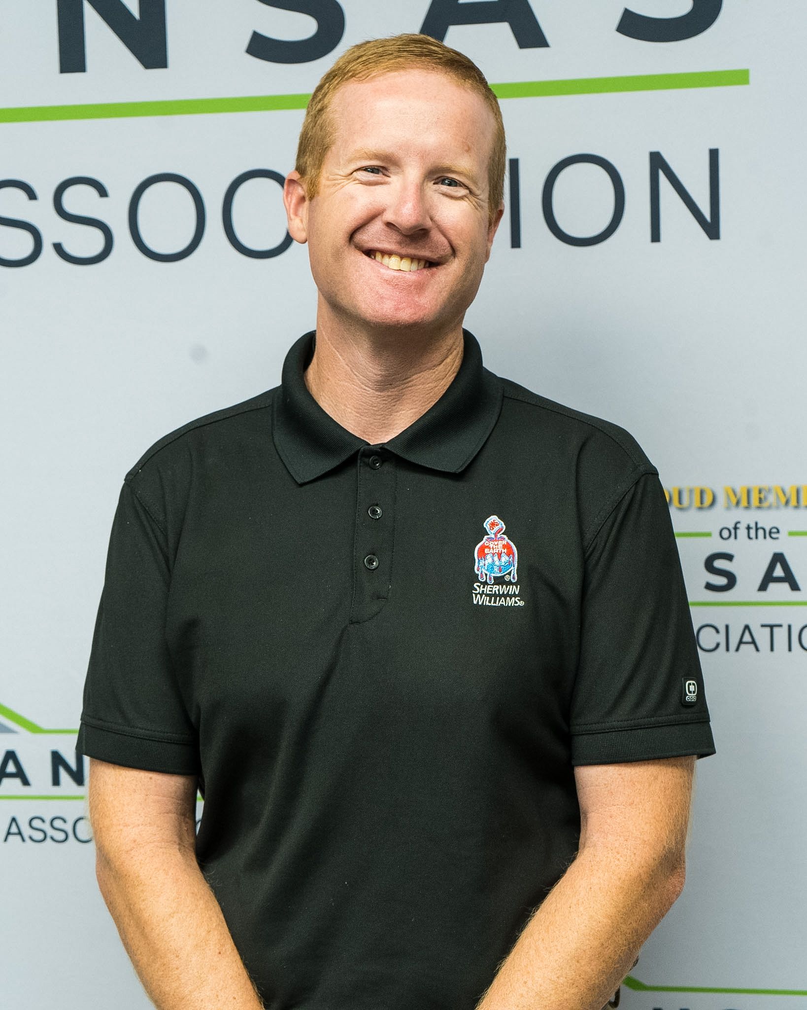 Smiling man in a dark polo shirt standing before an NSA association backdrop