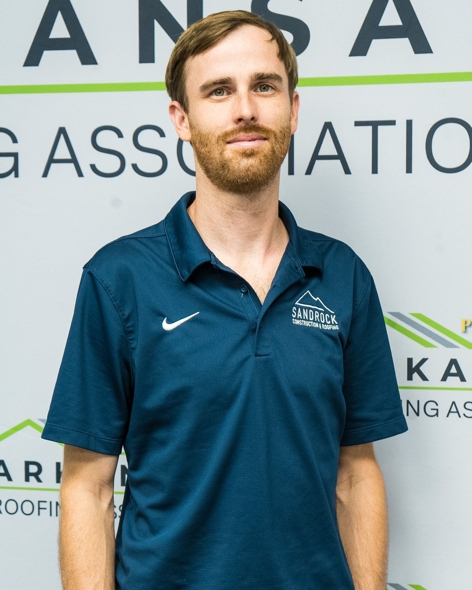 Man in a blue polo shirt standing in front of a branded event backdrop