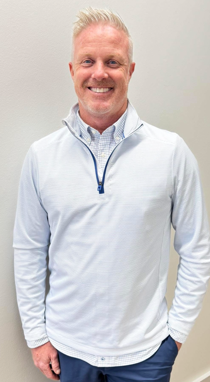 Smiling man in a white quarter-zip pullover standing against a plain wall