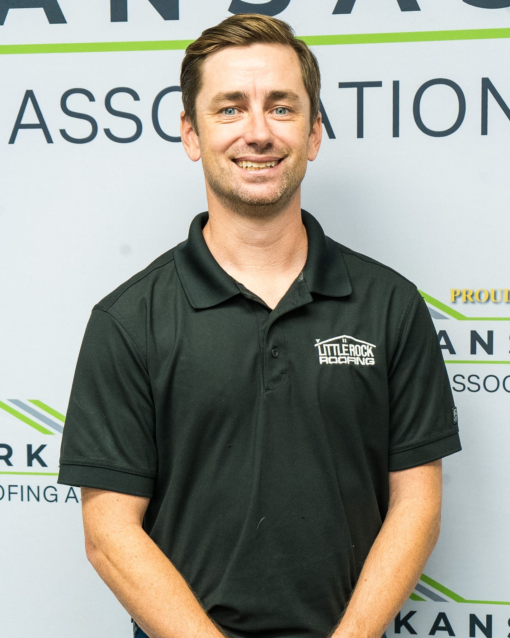 Smiling man in a dark polo shirt standing in front of an association backdrop
