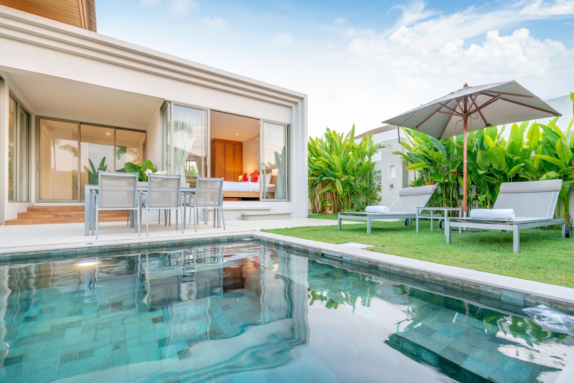 home or house Exterior design showing tropical pool villa with greenery garden, sun bed, umbrella, pool towels.