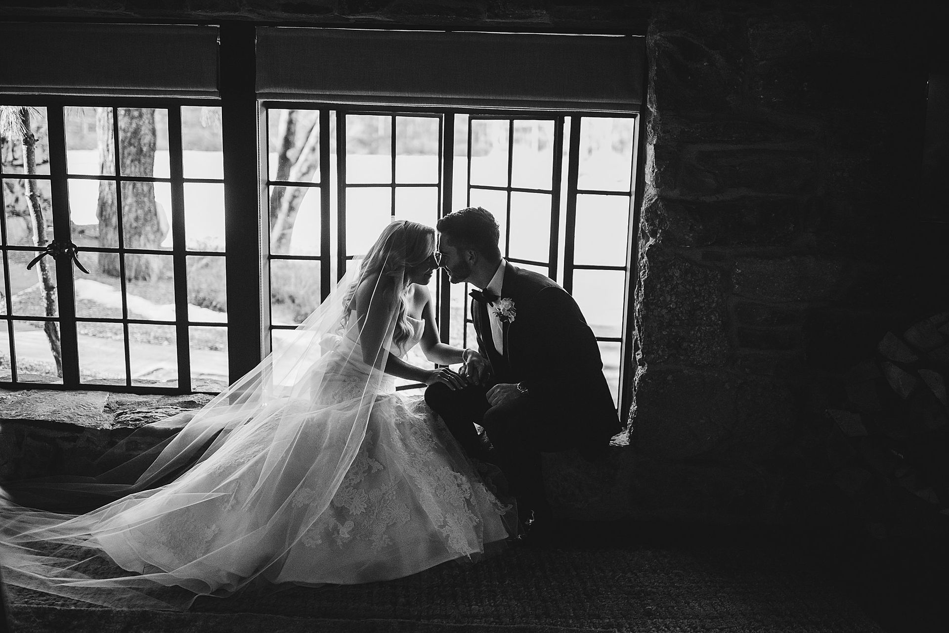 Bride and groom share a moment, their heads touching, by a window. Black and white.