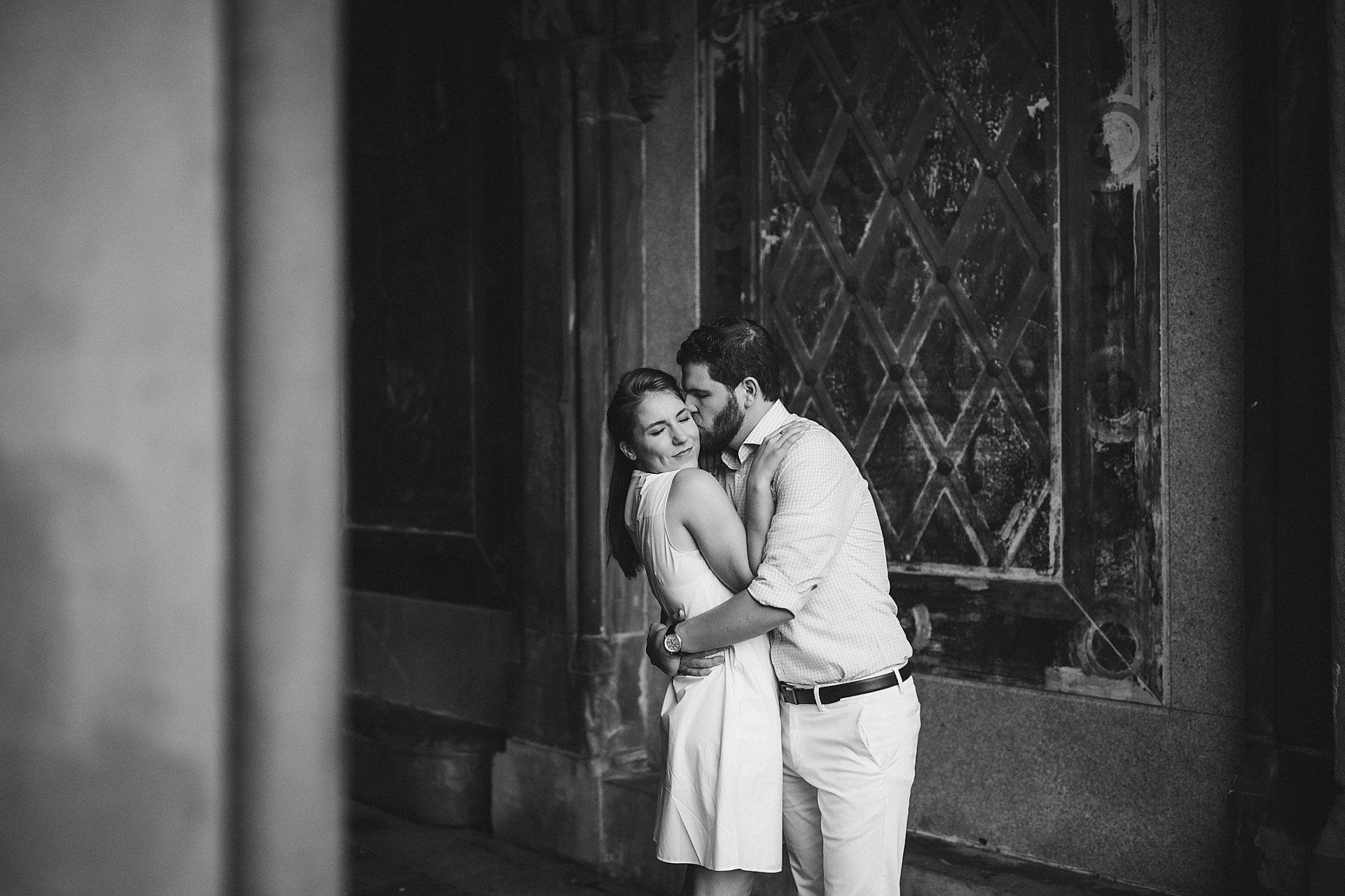Couple embraces near a window. Man kisses woman's cheek. Black and white photo. NYC