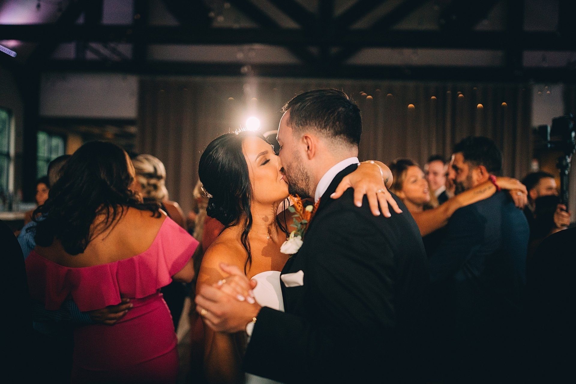 Bride and groom kissing on a dance floor, surrounded by guests.