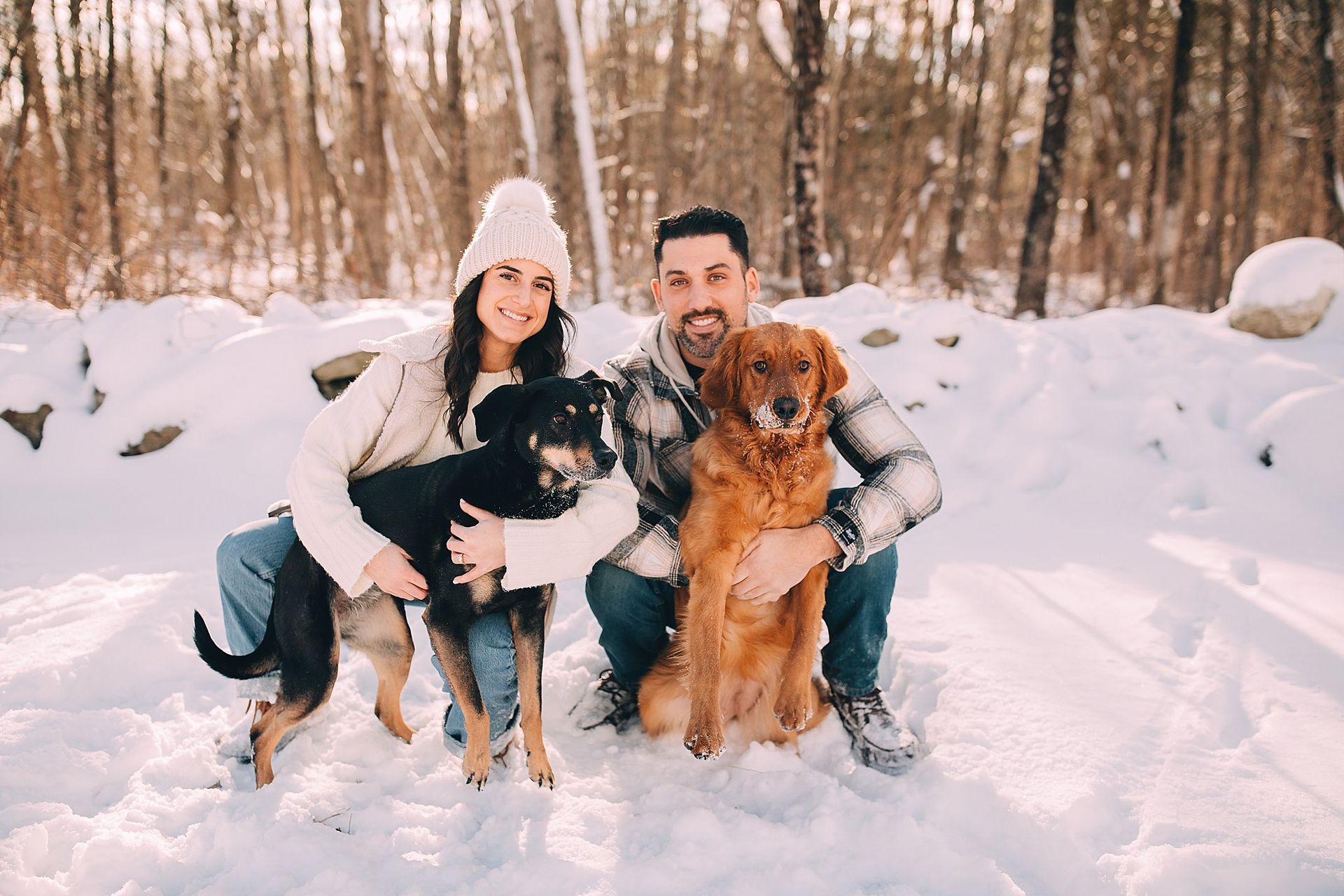 Couple with two dogs in snowy woods, smiling. Hudson Valley photographer