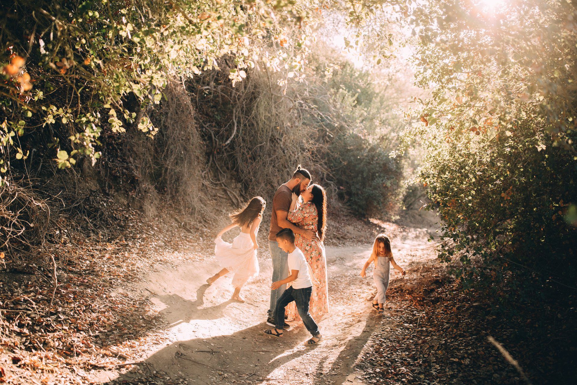 Family playing in sunlit forest clearing, kicking up leaves.