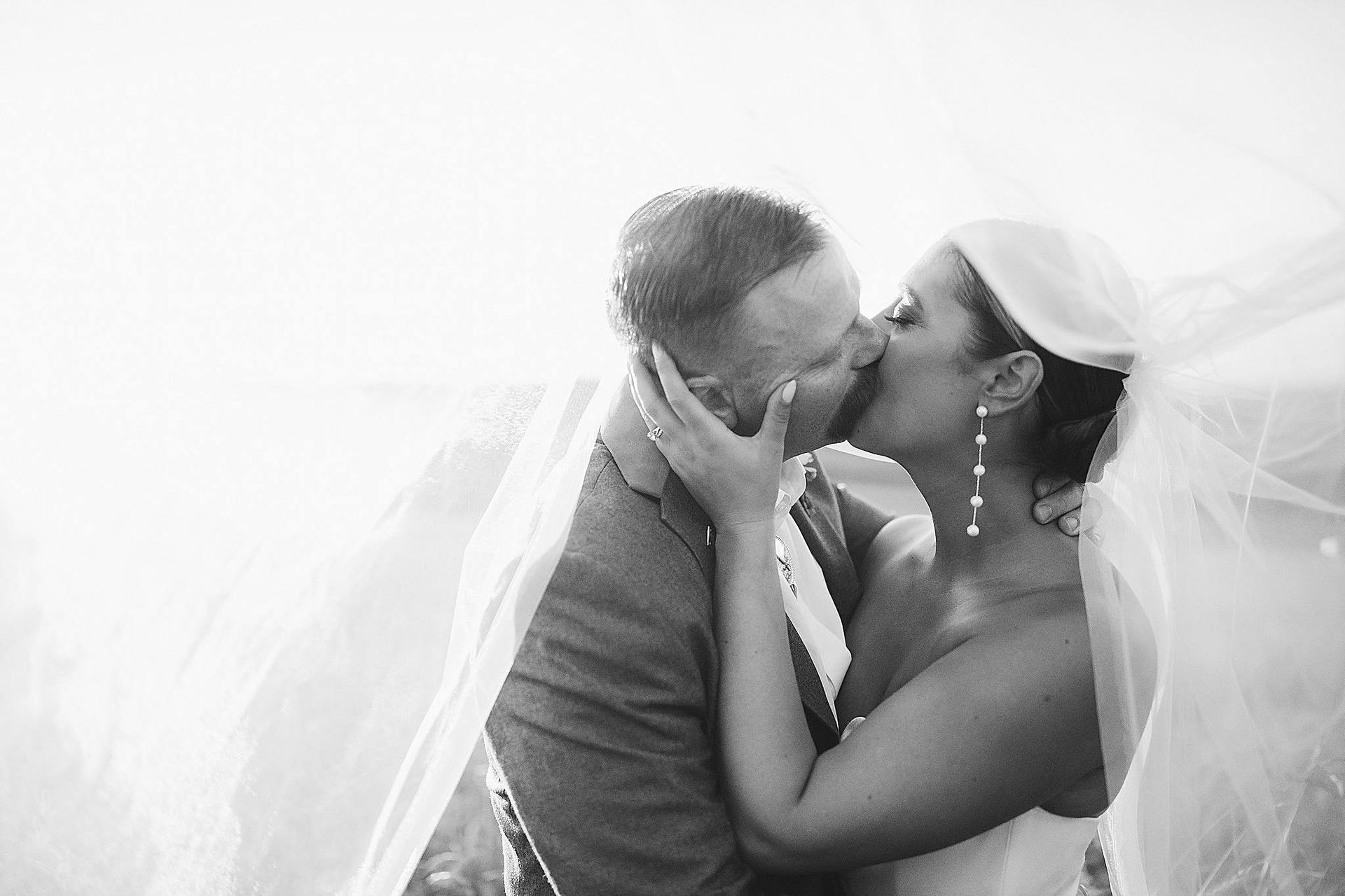 Bride and groom kissing, veil blowing in the wind.