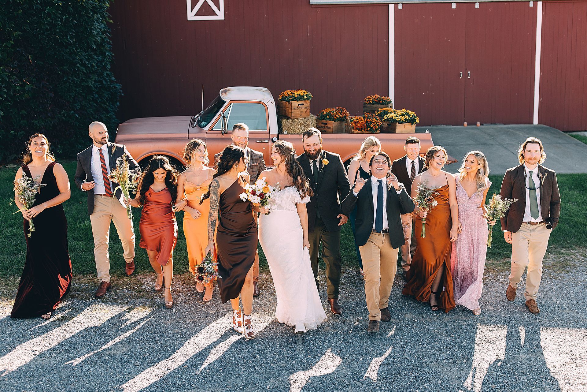 Wedding party posing in front of a red barn; bride and groom kissing, others smiling.