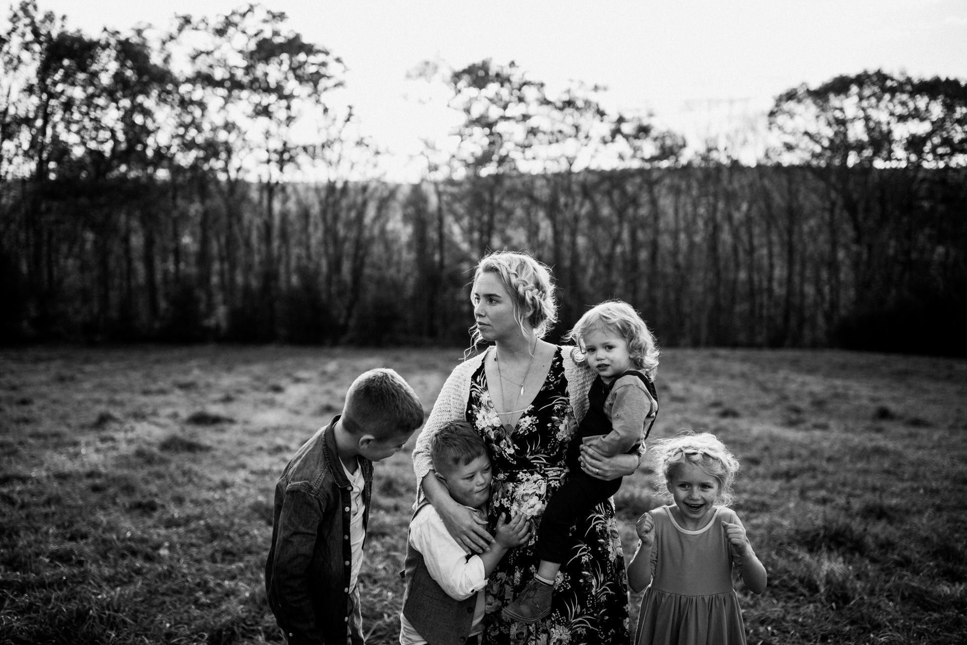 Woman and children in field; woman holding one child, others standing near; trees in background.