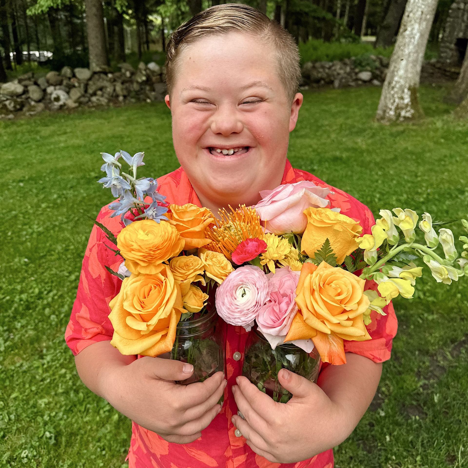 Person with Down syndrome holding two jars of colorful flowers outdoors, smiling.