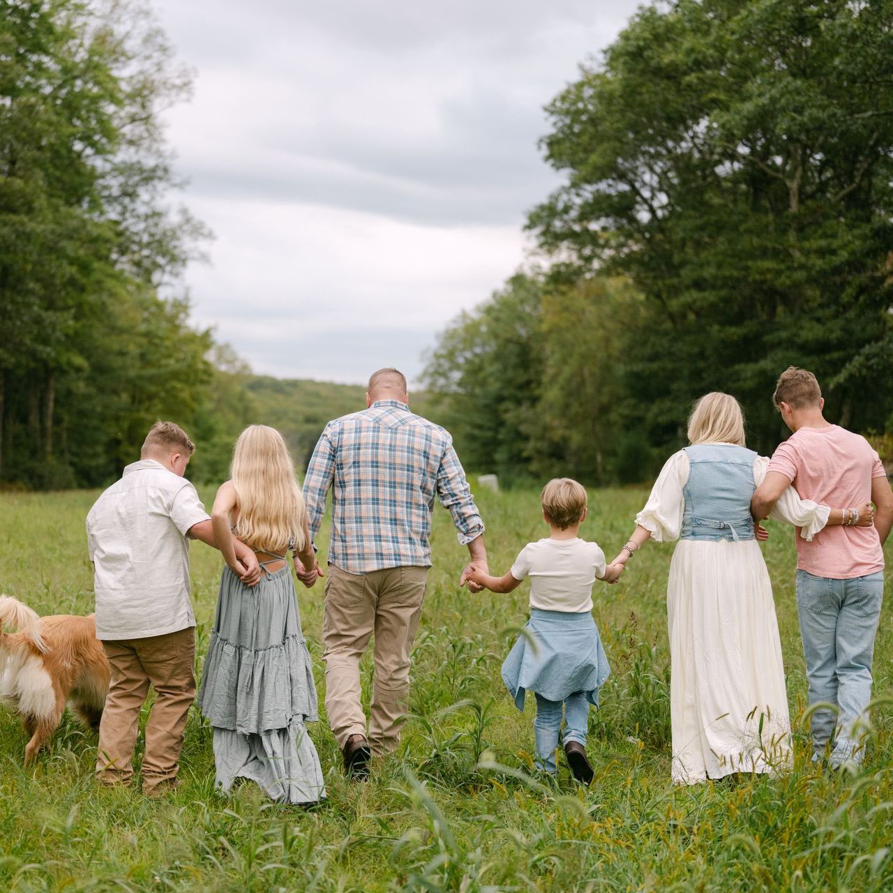 Family of six and a dog walk hand-in-hand through a grassy field.